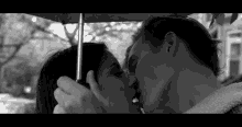 a man and woman are kissing under an umbrella .