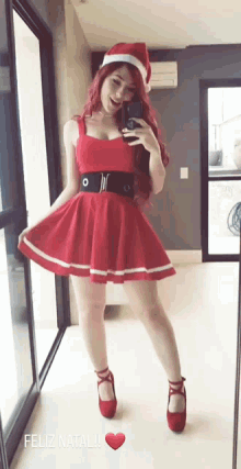a woman in a red dress and santa hat takes a selfie in front of a mirror