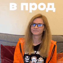 a woman wearing glasses and an orange jacket is sitting on a couch in front of a sign that says в прод