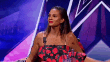 a woman in a red and black floral dress is sitting in front of a microphone on a stage .
