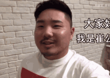 a man with a beard is smiling in front of a brick wall with chinese writing on it