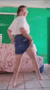 a woman in a white shirt and blue shorts is dancing in a room .