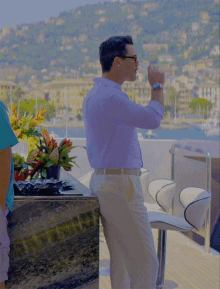 a man in a blue shirt and white pants is drinking from a glass