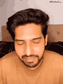 a man with a beard is sitting on a bed with his eyes closed ..