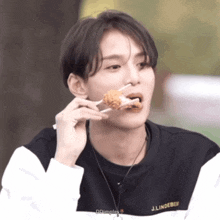 a man wearing a j.lindeberg sweatshirt is eating a piece of fried food