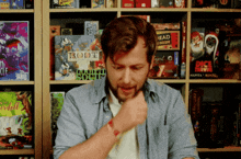 a man is sitting in front of a shelf full of board games including root