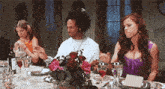 a group of people are sitting at a table with wine glasses and plates and flowers .