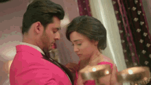 a man in a pink suit is adjusting the tie of a woman in a red dress