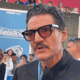 a man with glasses and a mustache stands in front of an advertisement for fantastic