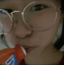 a woman wearing glasses is drinking from a bottle that says b