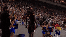 a football player stands in front of a crowd of cheerleaders and a mascot that says ' uc ' on it