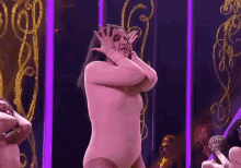 a woman in a pink bodysuit is covering her face with her hands