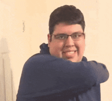 a man wearing glasses and a blue hoodie is standing in front of a wall .