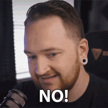 a man with a beard and ear plugs says " no " in front of a microphone