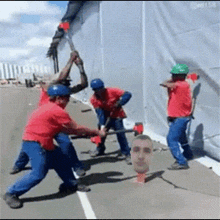 a group of construction workers are working on a wall with a picture of a man 's head behind them