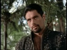a man with a beard is standing in a forest .