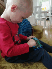 a young boy wearing a red spiderman shirt is playing a game on his tablet