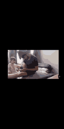 a man is sitting on a bed feeding a baby with a bottle