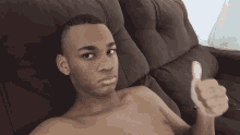 a shirtless man giving a thumbs up while sitting on a brown couch
