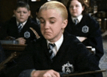 a boy in a suit and tie is holding a wand in a classroom with other students .