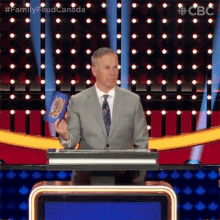 a man in a suit and tie is holding a book while standing at a podium on a television show .