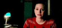 a woman in a red sweater is sitting in a dark room looking at the camera .