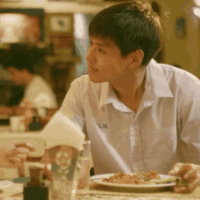 a young man sitting at a table with a napkin and a plate of food with the letter w on his shirt