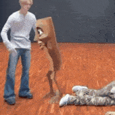 a man is standing next to a cartoon character on a wooden floor while a person is laying on the floor .