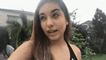 a woman in a black bikini is standing in front of a house and looking at the camera .