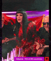 a woman in a red dress sits in front of a sign that says " albania 11th of 26 countries "