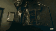 a man in a plaid shirt is standing in a dark room with a shadow of a hand on the wall .