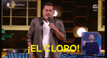 a man stands in front of a microphone with the words el cloro in yellow behind him