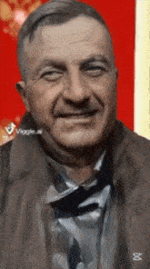 a man in a brown jacket is smiling in front of a red wall .