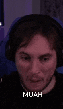 a man wearing headphones is making a funny face and the word muah is above him .