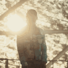 a man with dreadlocks is standing in front of a tree with the sun shining through it