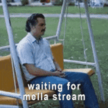 a man is sitting on a swing in a park waiting for mella stream .