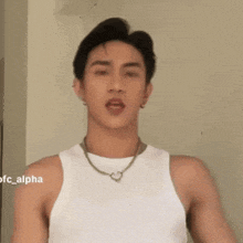 a man wearing a white tank top and a necklace with a heart on it