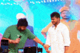 a man in a green shirt is holding a microphone and shaking hands with a man in a white shirt