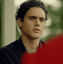 a man with curly hair is looking at the camera with a red background behind him .