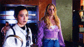 two women are standing next to each other in a room with a man in the background