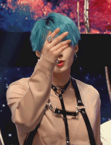 a man with blue hair and a ring on his finger covers his face