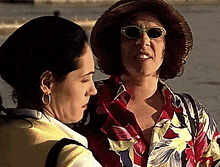 a woman wearing sunglasses and a straw hat talks to another woman