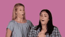 two women are standing next to each other on a pink background and one of them is pointing at the other .