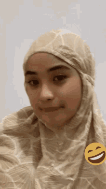 a woman wearing a hijab is smiling with a smiley face next to her .