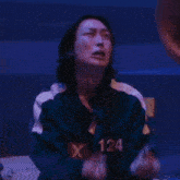 a woman in a green jacket is praying in a dark room with her hands folded .