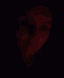 a woman is covering her mouth with her hand in a dark room with a red light behind her .