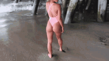 a woman in a pink one piece swimsuit is standing on a beach under a pier .