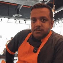 a man wearing a black shirt and an orange apron with the letter s on the front