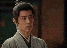 a man with a bun on his head is wearing a kimono and looking at something .