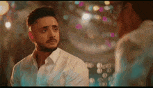 a man in a white shirt looks at himself in the mirror